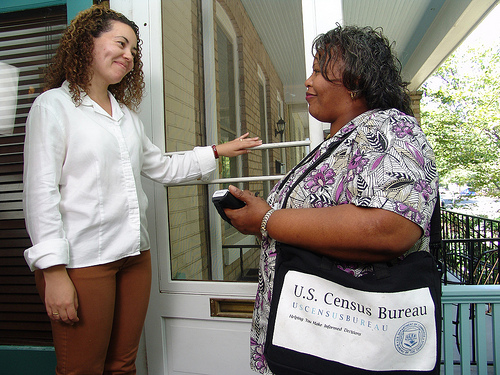 A woman with a US Census bag stands outside the home of another woman, who has opened the door.