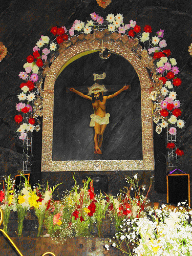 Painting of crucified Jesus on a black stone, surrounded by a gilded frame and red and white flowers