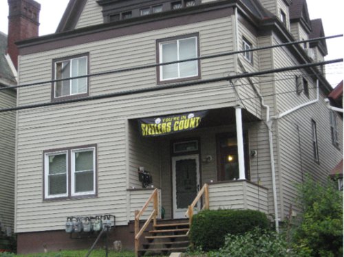 A three-storey house with gray siding has a black banner over its porch, which reads 'You're in STEELERS COUNTRY'